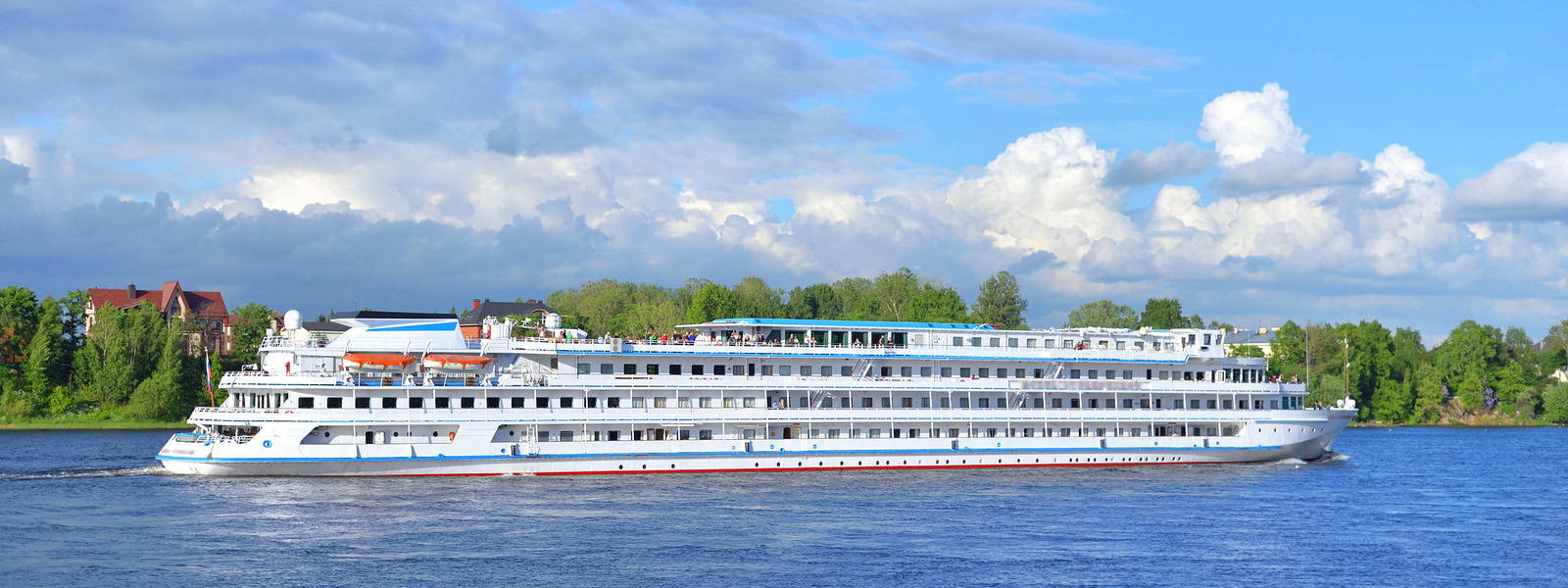 A river cruise vessel passing a hillside village and vineyards